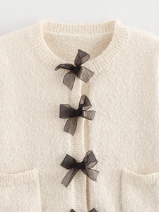 Detail view of beige knitted cardigan with black mesh bows and textured boucle fabric
