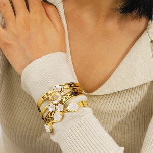 Mehrlagige goldene Blumenarmbänder mit weißen Emaille-Blüten und Sternprägung auf Strickstoff