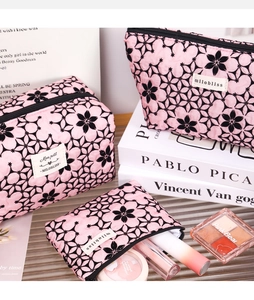 Three-piece pink floral quilted makeup bag set with zipper closures on glass stand