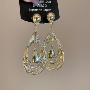 Macro detail of gold-plated layered teardrop earrings with central hollow droplet