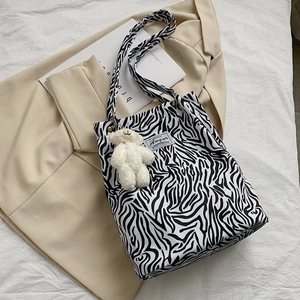 Detail of zebra pattern canvas tote with a white plush bear charm on a beige blazer