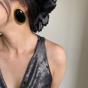 Close-up of vintage black oval earrings with a gold frame worn by a female model