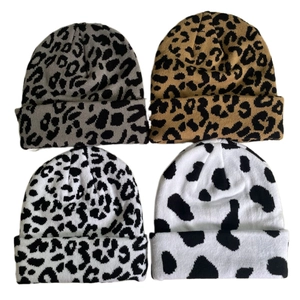 Flat lay of four knit beanies with leopard and cow patterns on a white background