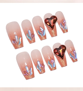 Detail of long ballerina nails with orange gradient glitter and red heart gemstones