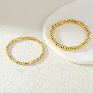 Detailed view of two 18K gold plated polished round bead elastic bracelets on ceramic plate
