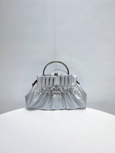 Close-up of silver pleated evening bag featuring a sparkling rhinestone floral clasp detail