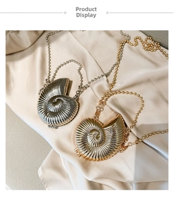 Detail of shell-shaped metallic crossbody bags in gold and silver on cream silk fabric