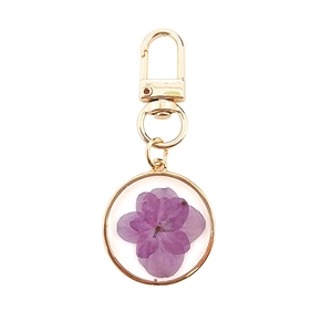 Detail of a round resin keychain featuring a real purple dried flower with a gold border