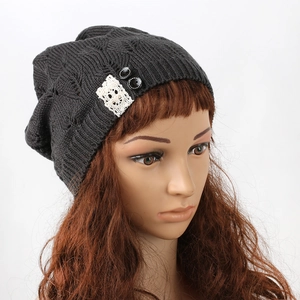Detail view of women's grey knitted beanie featuring lace patch and hollow leaf patterns