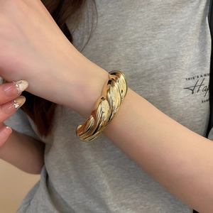 Close-up of a gold chunky twisted cuff bracelet with a glossy mirror metallic finish on wrist