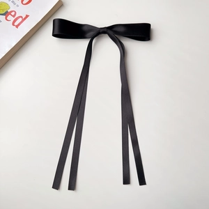 Detail of a black satin ribbon bow hair clip with long streamers on a white background