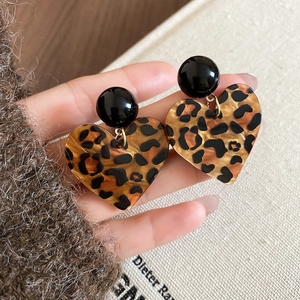 Nahaufnahme von herzförmigen Leopard-Ohrringen mit schwarzen Kugelsteckern in der Hand