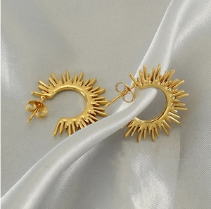 Detailed macro shot of golden sunburst fan-shaped earrings on elegant grey silk fabric