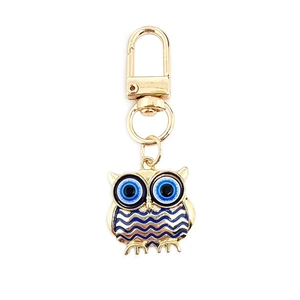 Close-up of golden owl keychain with blue evil eye pattern and lobster clasp detail