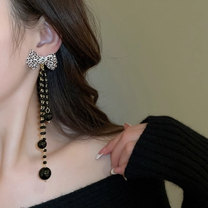 Detail of leopard print bow earrings with long golden tassels and black beads on model
