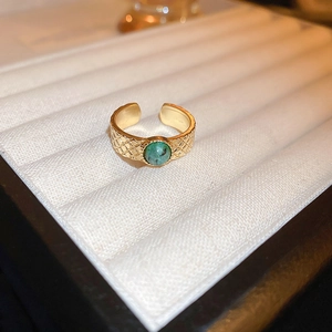 Detail of adjustable gold dragon ring with green stone and quilted metal band texture