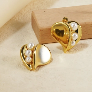 Vue macro de boucles d'oreilles cœur dorées avec trois perles blanches sur socle en bois