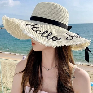 Wide brim straw hat with Hello Sunshine embroidery and black ribbon on a sunny beach