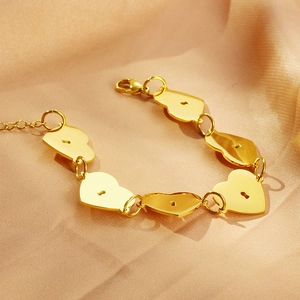 Détail d'un bracelet cœur plaqué or 18 carats avec motif de serrure sur tissu de soie beige