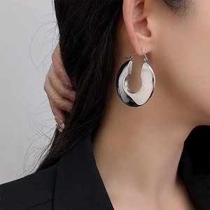 Macro detail of large chunky silver C-shape metal hoop earring worn by a model