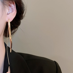 Detail of long gold teardrop pendant earring on model with minimalist modern style