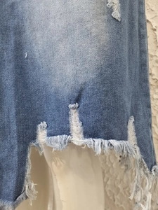 Close-up of distressed denim skirt showing ripped holes and frayed hem details