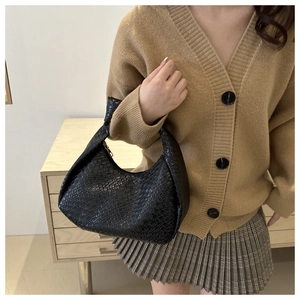 Detail of black woven shoulder bag with knotted handle and textured faux leather finish