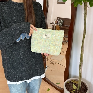 Close-up of green tweed makeup bag texture with decorative white woven label