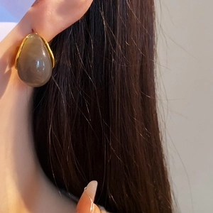 Detailed close-up of a brown resin water drop earring with elegant golden metal frame