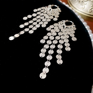 Detailed view of silver sequin tassel earrings on black velvet with pearl accents