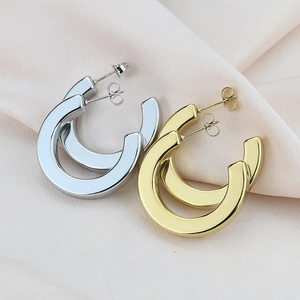 Close-up of gold and silver chunky C-shaped geometric earrings on pink silk fabric