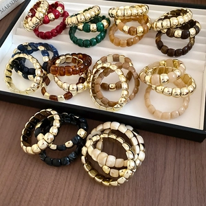 Chic acrylic and gold metal beaded stretch rings in various colors on a display tray