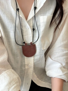 Close-up of a vintage brown faux leather magnetic glasses holder pendant on a necklace