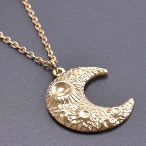 Macro detail of gold crescent moon pendant with embossed moon surface and sun totem texture