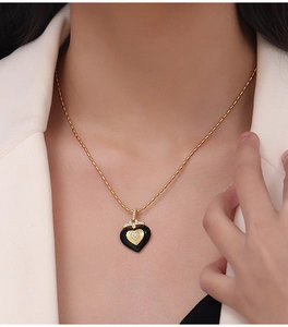 Detail of a gold-plated heart pendant with black enamel and zircons on a bean chain