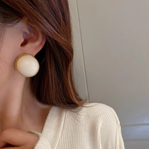 Close-up of cream white acrylic dome earring with gold textured rim on model