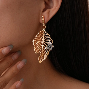 Detail of gold metal hollow leaf earring with small silver flower on model's ear