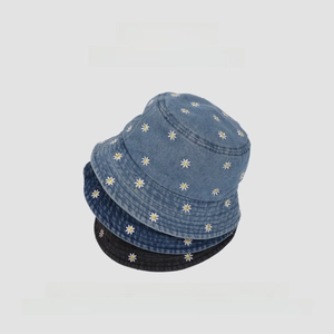 Vertical stack of three denim bucket hats with daisy embroidery in light blue, mid blue and grey