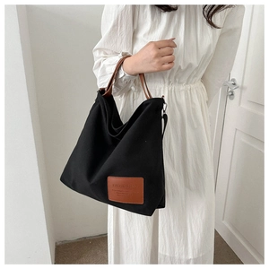 Close-up of black canvas tote bag showing the texture and brown leather handle detail