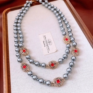 Detail view of vintage double-layer grey pearl necklace with gold charms and red crystals