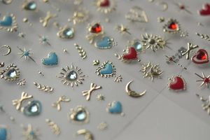 Close-up of nail art stickers featuring gold sun, moon, and heart shapes with gems