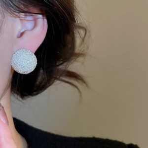 Close-up of silver-tone chunky textured round stud earrings worn by a model