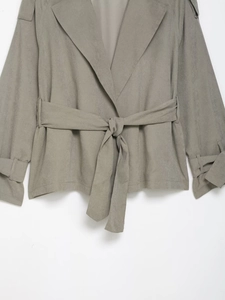 Detail of grey-green lapel jacket featuring waist tie, epaulets and buckled cuffs