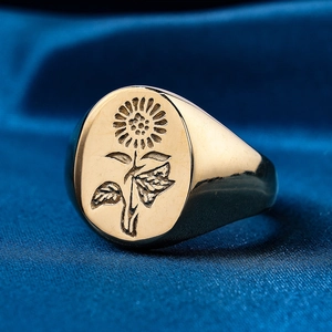 Macro shot of gold stainless steel signet ring with sunflower engraving on blue silk