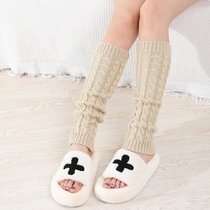 Close-up of khaki knit leg warmers with cable pattern and plush slippers in cozy home setting