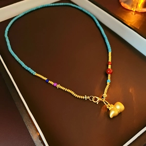 Detail of gold-plated gourd pendant necklace with turquoise and colorful beads in a box