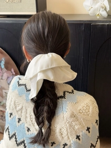 Model view showing a large white glossy satin scrunchie styled in hair in a cozy home setting