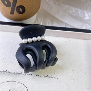 Macro shot of a matte black hair claw clip featuring five elegant white pearls on top