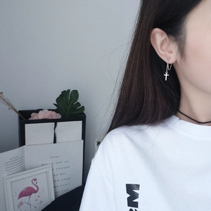 Close-up of silver cross earring with delicate chain on model in minimalist setting