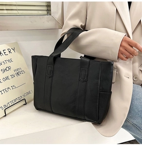 Detail of a large black faux leather tote bag held by a model in a minimalist blazer